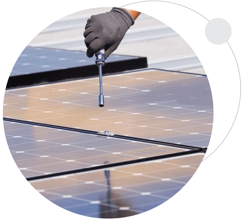 A person holding a screwdriver on top of a solar panel.