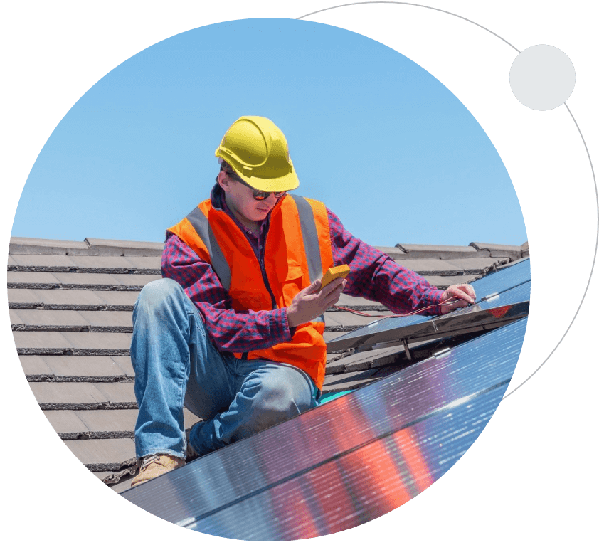 A man in an orange vest and hard hat on top of a roof.